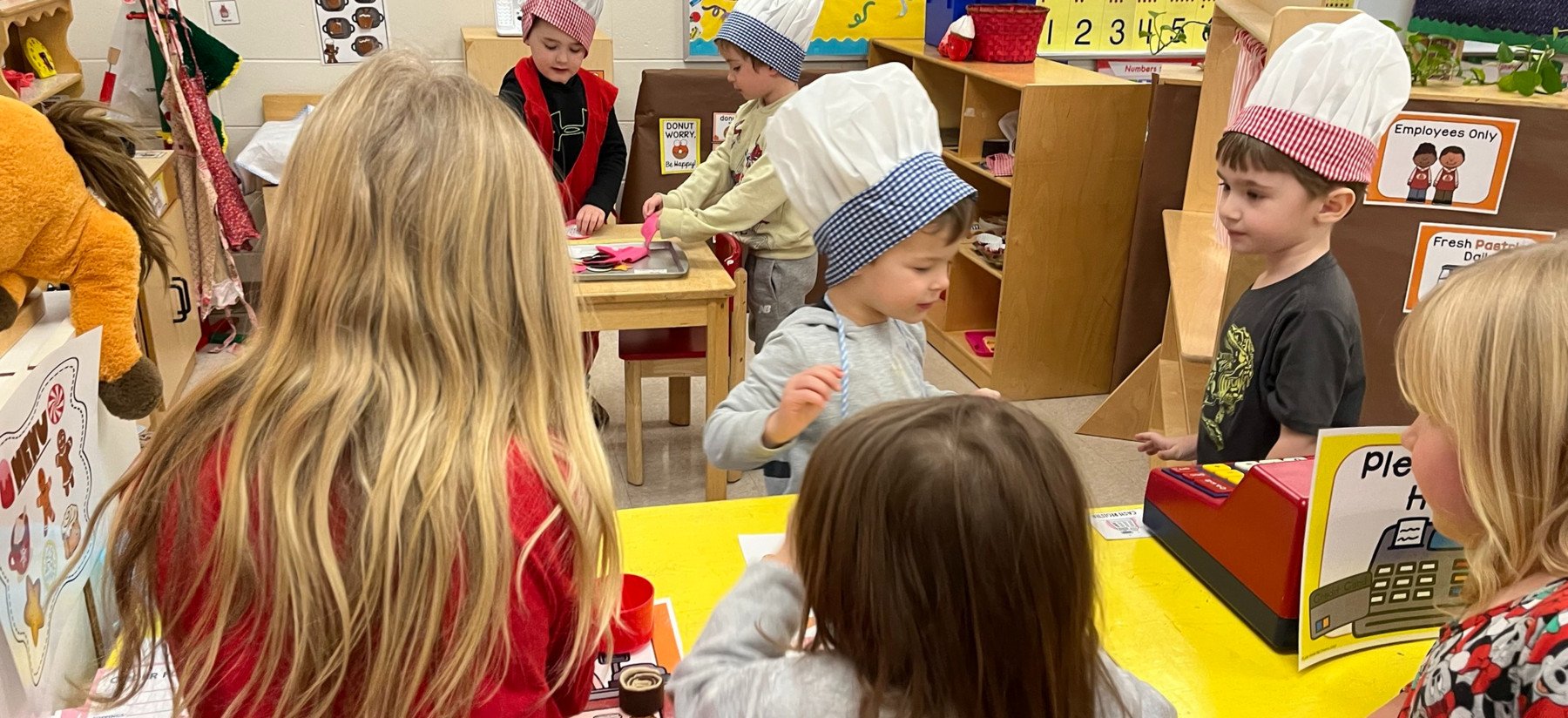 Pre-K students in chefs hats pretending in a bakery